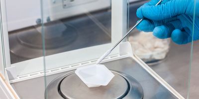 Gloved hand of scientist weighing out a sample on an analytical balance