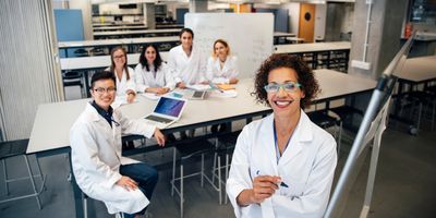 A mixed race female teacher and students smile for a portrait, they are in a laboratory classroom