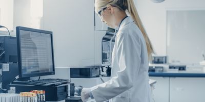 female researcher in biotech lab analyzing samples in front of computer