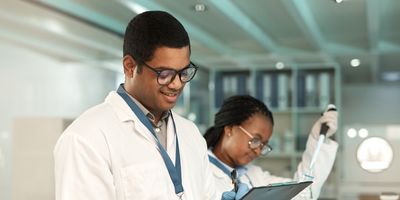 Shot of a young scientist writing notes while working alongside a colleague in a lab