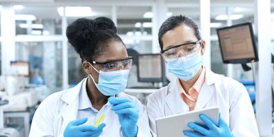 Female medical researchers discussing over tablet PC while working in laboratory