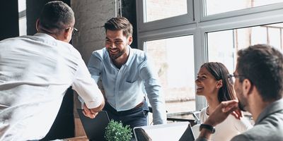 Young modern men in smart casual wear shaking hands and smiling while working in the creative office