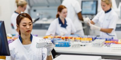 Female scientist looking at sample tubes in lab with others working in the background