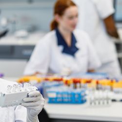 Female scientist looking at sample tubes in lab with others working in the background