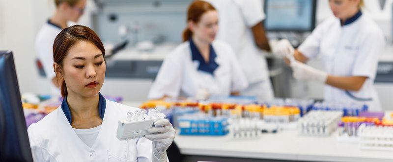 Female scientist looking at sample tubes with others working in the background