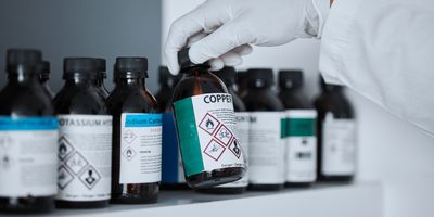 Gloved hand reaching for chemical bottles in lab