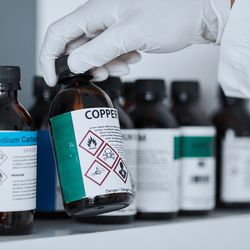 Gloved hand reaching for chemical bottles in lab