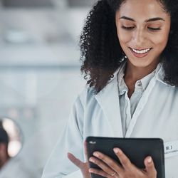 Female researcher in white lab coat and dark curly hair using a tablet in a lab setting