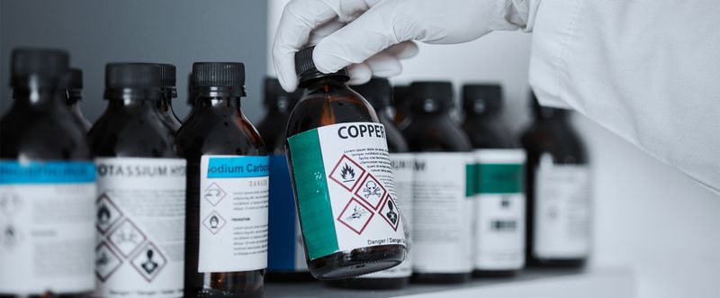 Gloved hand reaching for chemical bottles in lab