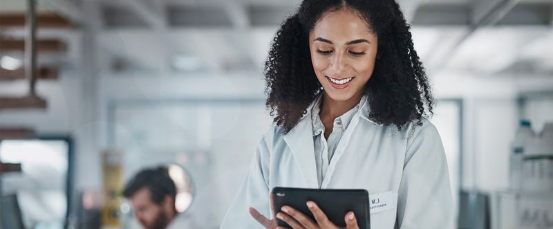 Female scientist in white lab coat using tablet in lab setting