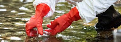 a scientist in a river collecting water samples for environmental testing