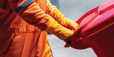 Man in protective suit pushing red disposal container for Infectious waste.