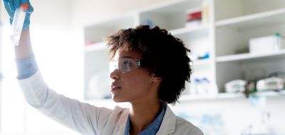 A woman in a bright lab holds a falcon centrifuge tube up to the light for visual inspection