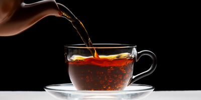 Black tea being poured into glass teacup