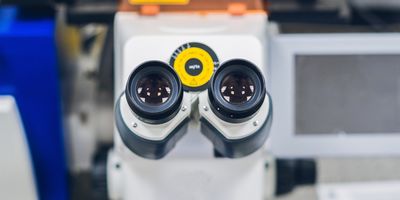 a head-on view of the eyepiece of a confocal microscope with an out of focus lab bench in the background