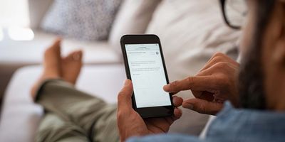 Man resting on a couch at home checking his email on his phone