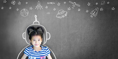 A young girl backed against a chalkboard with drawing relevant to STEM on it