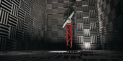 A dark grey acoustic anechoic chamber with a turbine mounted on a red tower structure in the center of the room.