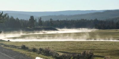 a photo of mist over a small river running through a field, illustrating that in the process of evapotranspiration, moisture becomes visible in a saturated layer of air near the land surface