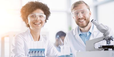 Two scientists wearing safety glasses smile at the camera