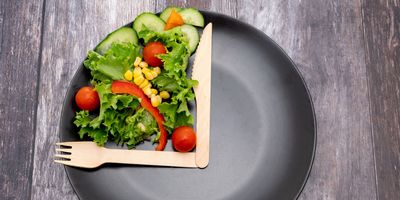 Fork, plate, and salad arranged on a plate to resemble a clock