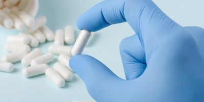 A gloved hand holding a pill with spilled pills in the background