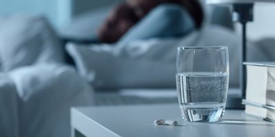 Person in bed with pills and glass of water on a nightstand