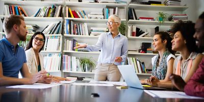 Team of colleagues sitting at a table with female leader standing at the head directing conversations