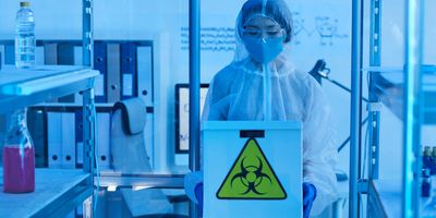 Young woman in protective workwear holding box with chemicals working in the laboratory