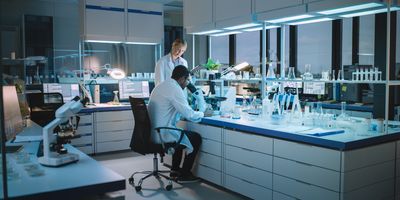 Male and female scientists talk while using microscope in modern lab