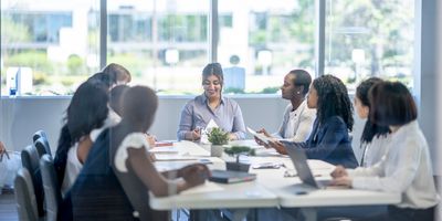 A small group of business professionals sit around a boardroom table as they meet to discuss new strategies.