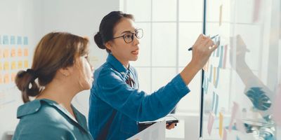 Manager writes notes on a whiteboard while employee watches