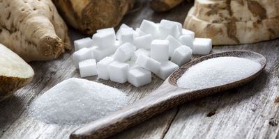 Spoon full of white sugar next to sugar cubes on a table