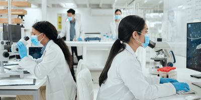 Two female scientists work at microscopes in the lab