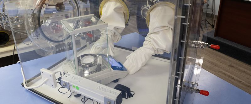 Scientist weighs sample on an analytical balance in a glove box