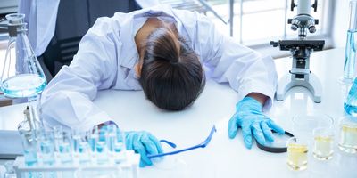 Scientist woman feeling upset and stressed, laying here head on her lab bench