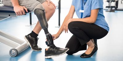 Man with prosthetic leg sits on bench with physical therapist next to him