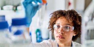 Female scientists in lab coat and PPE looking at a test tube