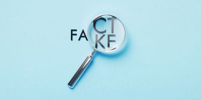 A magnifying glass over the words "Fact" and "Fake" on a blue background