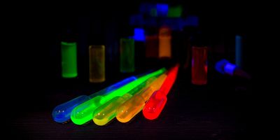 Four plastic pipettes with fluorecent quantum dots in them of different colors in a dark room