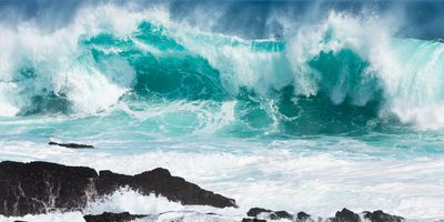 large ocean waves crashing against dark black rocks with lots of white spray coming off of the turquoise water