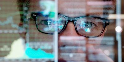 A closeup of a man's face with reflections of a computer screen on it to illustrate the concept of lab monitoring.