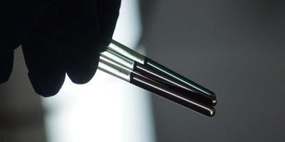 a shadowy photo of a hand holding three clear NMR tubes containing clear liquids