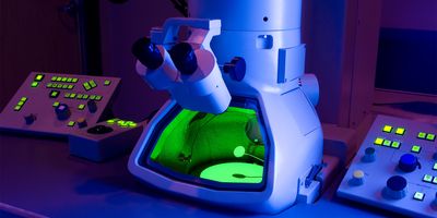 a scanning transmission electron microscope sits on a lab bench bathed in blue and purple light with the inside of the microscope glowing green