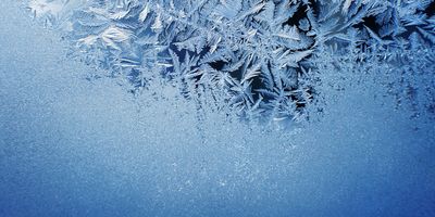 frost patterns on glass, light blue colored frost crystals with a dark background visible through the gaps in the crystals