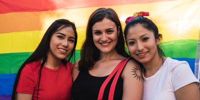 Three young women in front of a rainbow flag