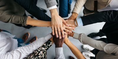 a diverse group of people's hands on top of each other in a circle, only arms and hands are visible, wearing business clothing