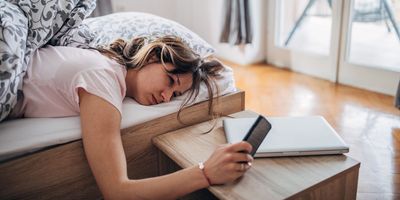 Young woman is waking up and looking at her smart phone